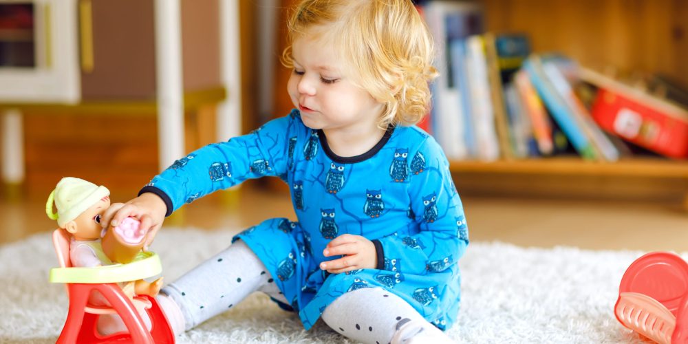 Adorable cute little toddler girl playing with doll. Happy healthy baby child having fun with role game, playing mother at home or nursery. Active daughter with toy