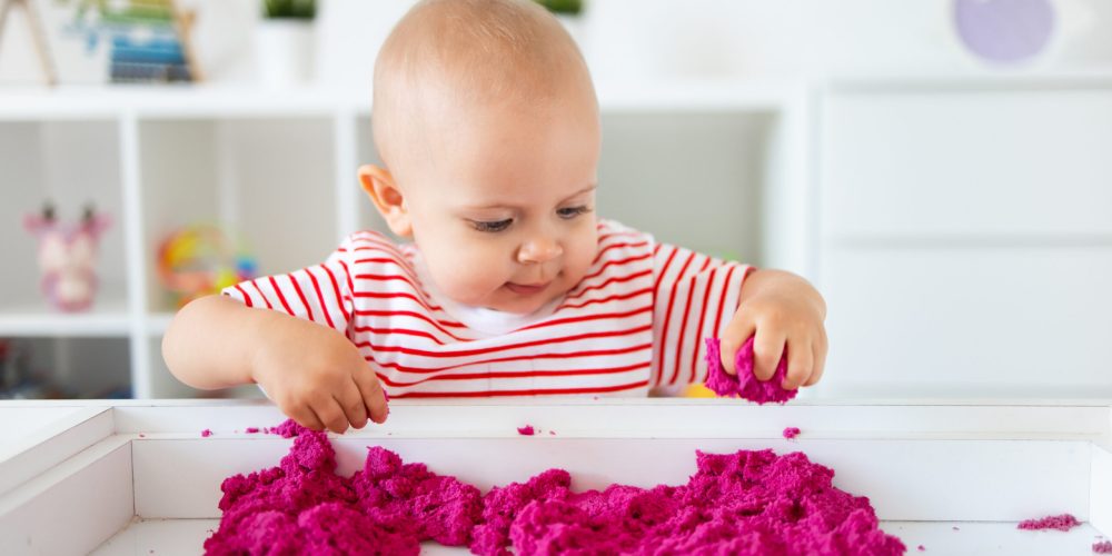 Baby playing with kinetic sand. Little girl playing with sand at home, games, education, children room