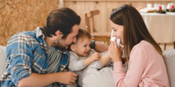 Young loving family playing with little small child kid son daughter toddler, hugging and embracing at home. Child care and parenthood concept