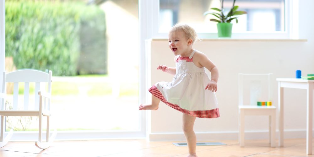 Happy blonde toddler girl having fun dancing indoors
